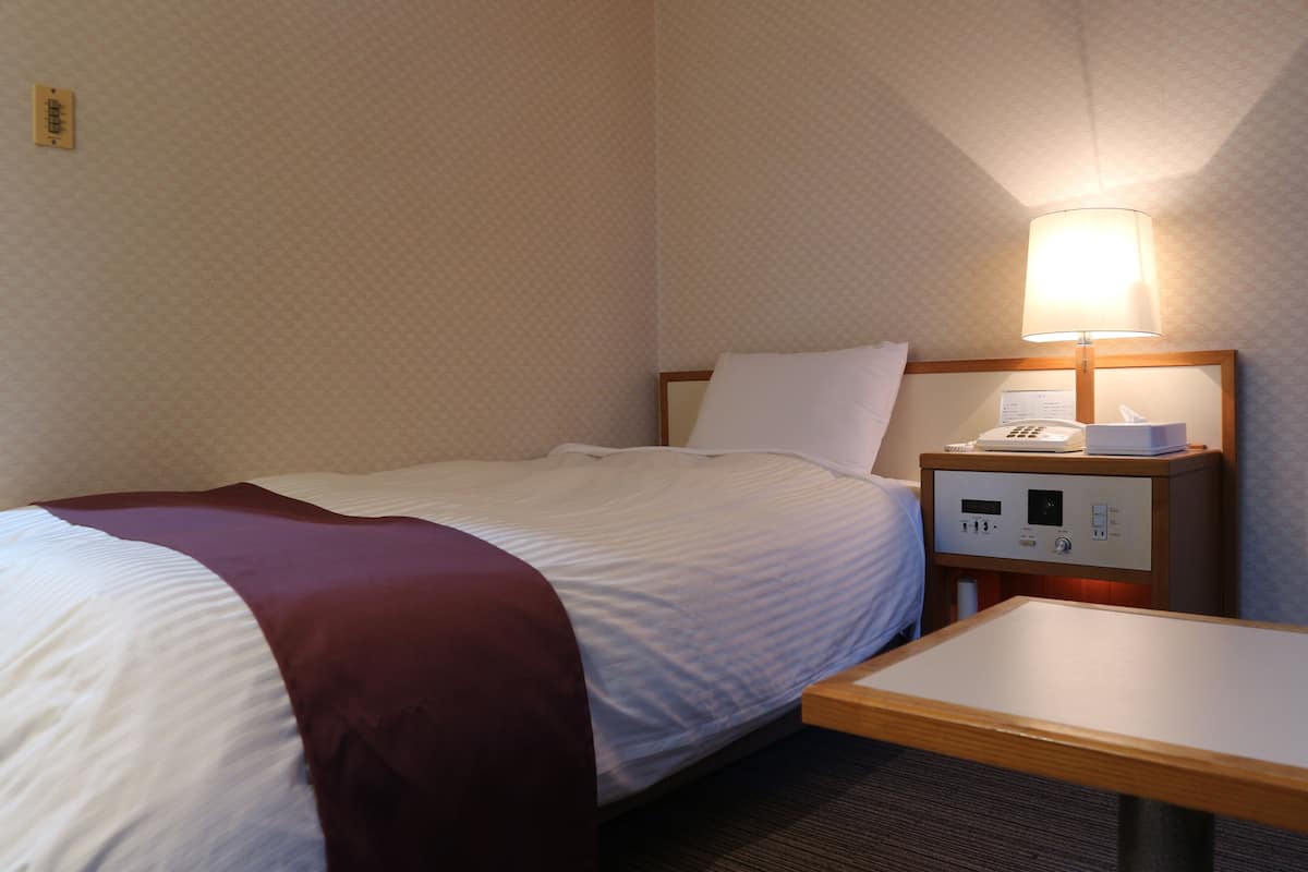 A hotel room with a bed, a bedside table, a lamp, and a control panel.