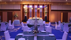 Un gran saló de banquets amb taules rodones preparades per dinar, caires blancs i centrals florals.