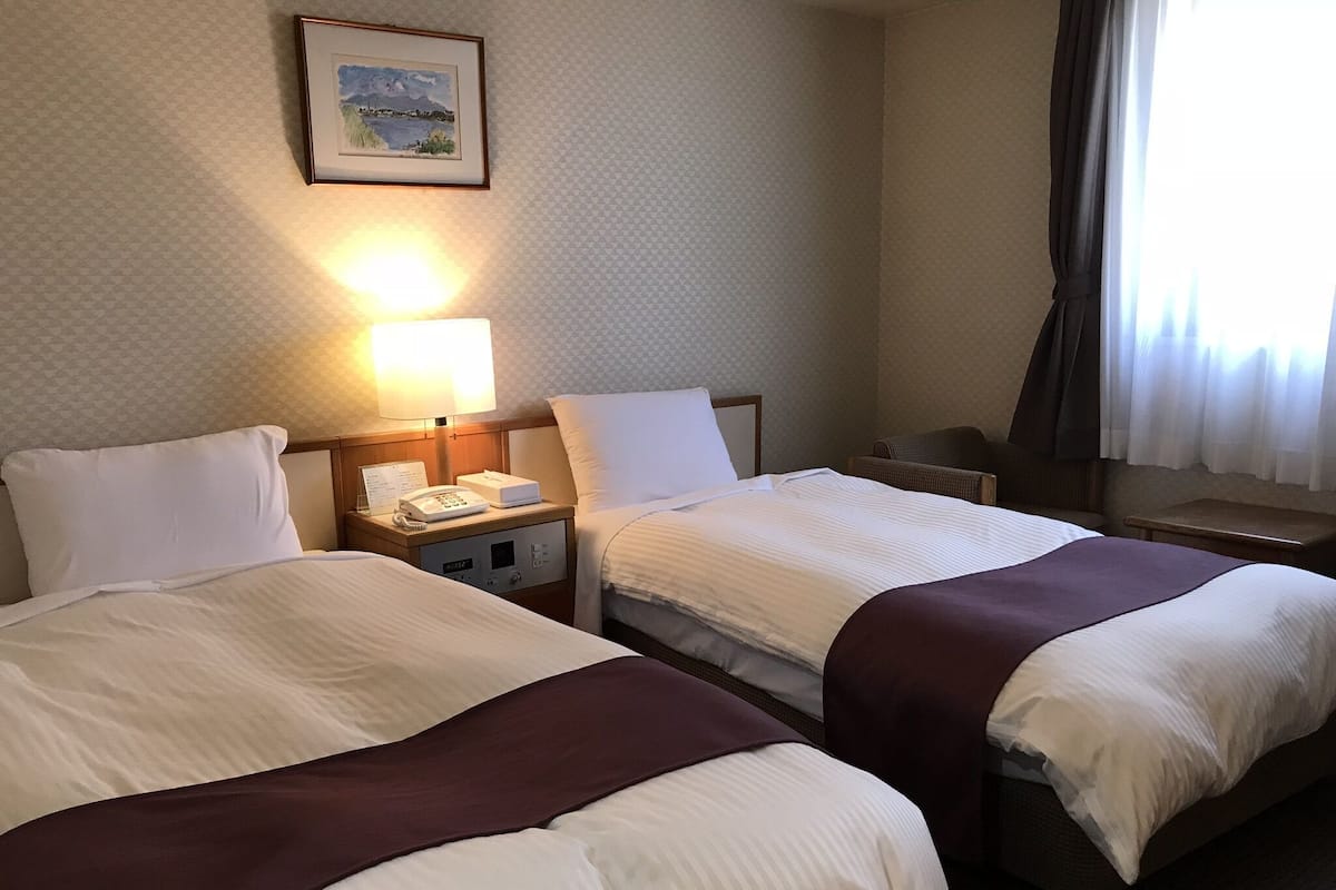 A hotel room with two beds, a nightstand with a lamp, a telephone, and a framed picture on the wall.