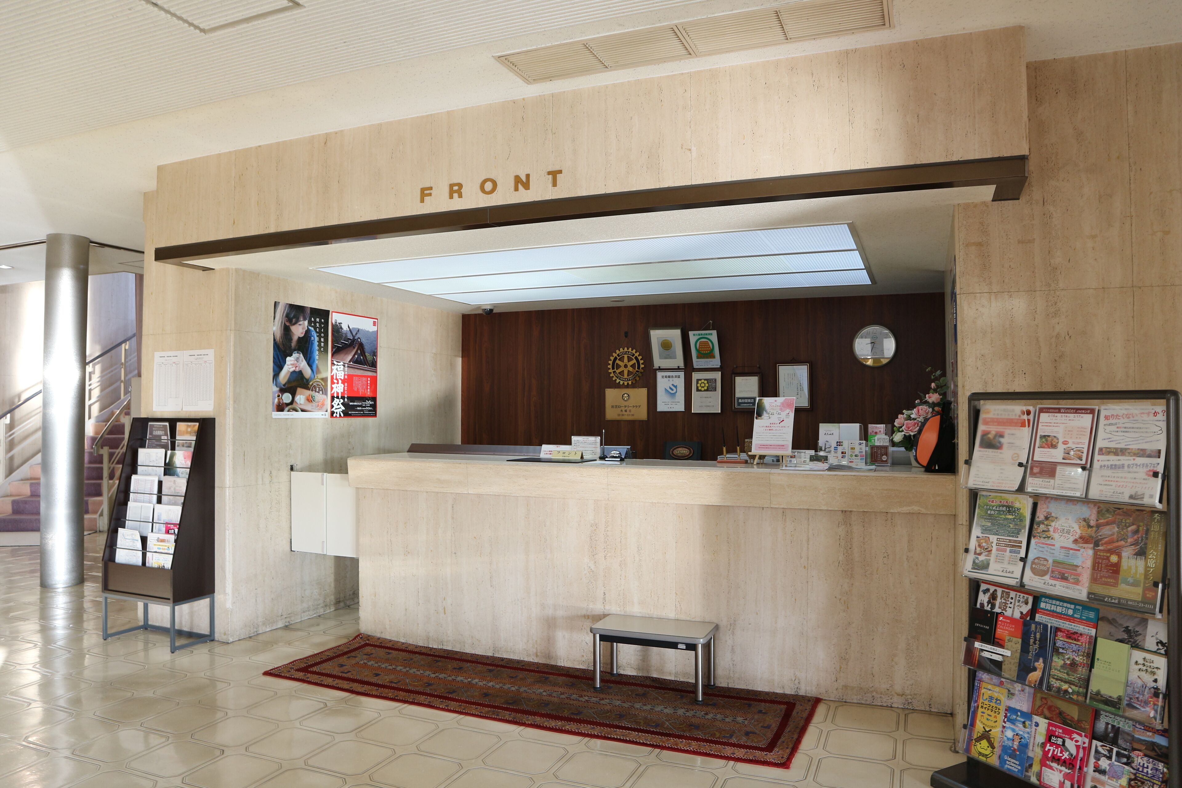 A reception desk with a 'FRONT' sign, a small bench, a bulletin board with various notices, and a magazine rack with brochures.