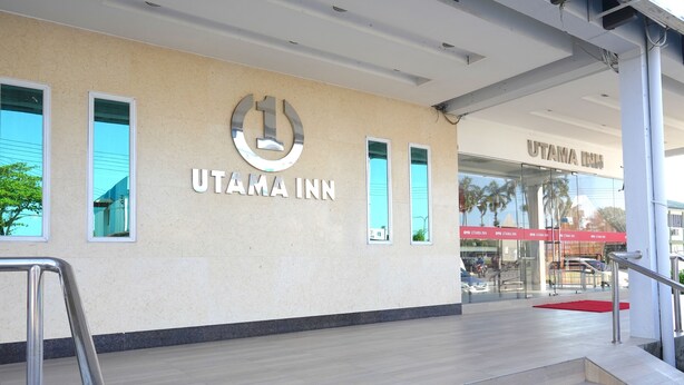 Das Hotel Utama Inn mit gut sichtbarem Logo, großen Fenstern und einer Treppe zum Eingang.