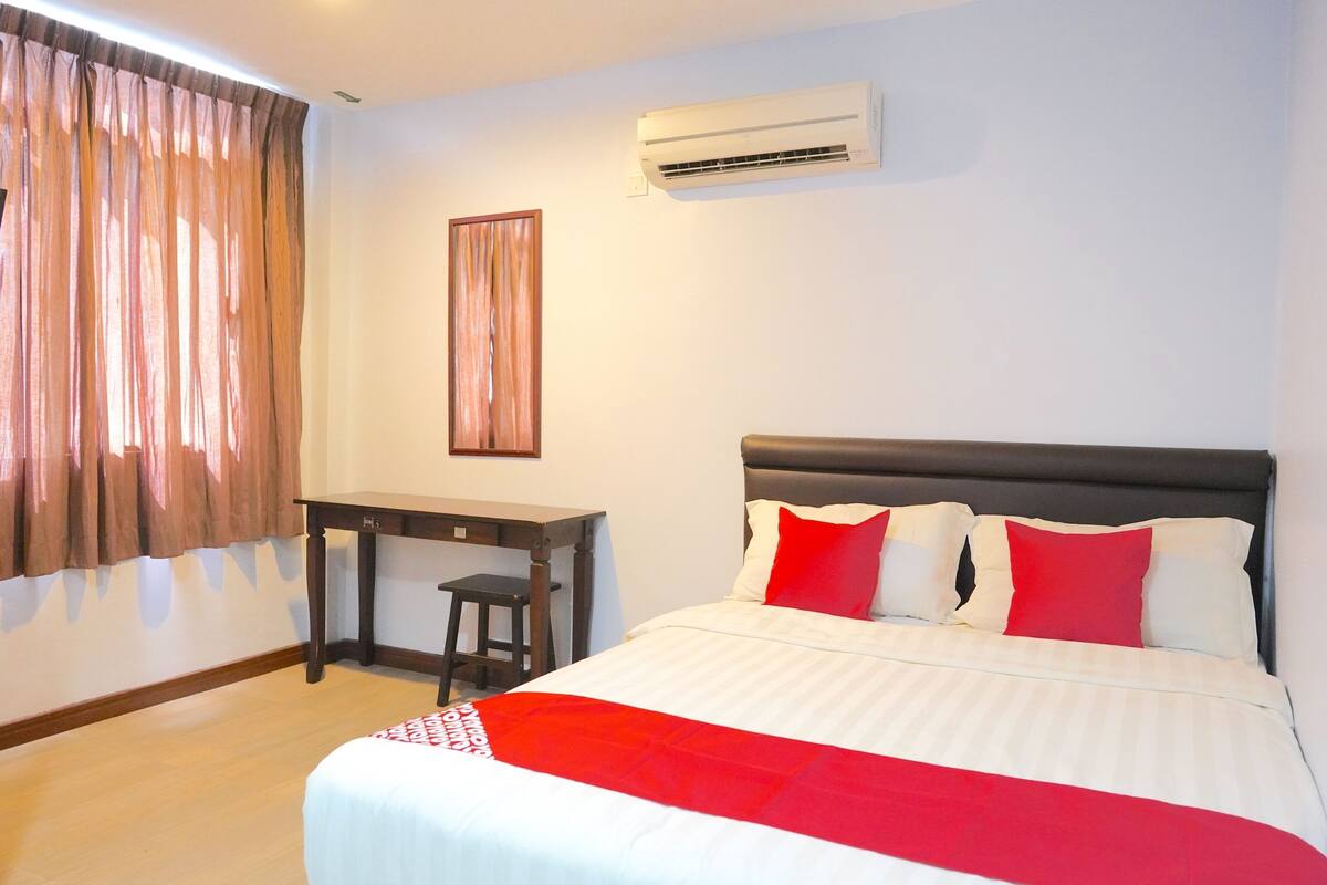 A bedroom with a bed, a desk, and an air conditioning unit.