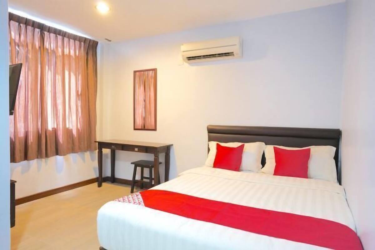 A bedroom with a bed, a desk, a chair, an air conditioning unit, and curtains.