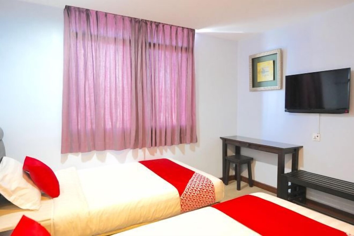 Une chambre d’hôtel avec deux lits, une télévision, un bureau et une fenêtre avec des rideaux.