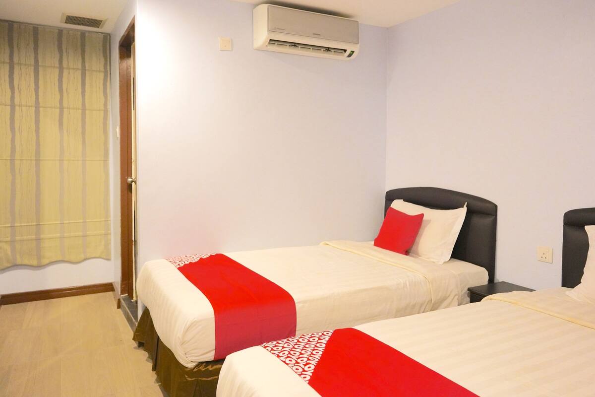 A hotel room with two beds, a window with curtains, an air conditioning unit, and a wooden floor.