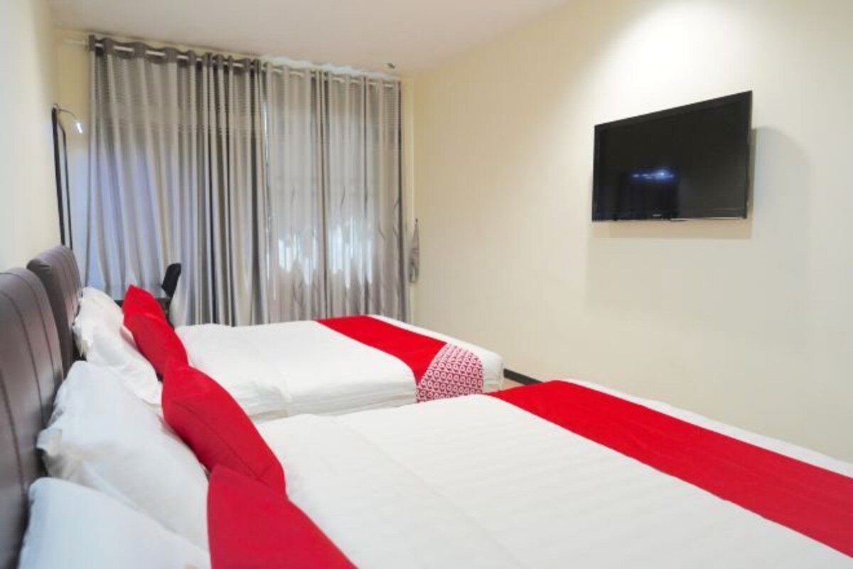 A hotel room with two beds, a flat-screen TV mounted on the wall, and a window with curtains.