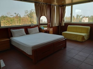 A bedroom with a large bed, a bedside table, a nightstand, a yellow sofa, and a window with curtains.