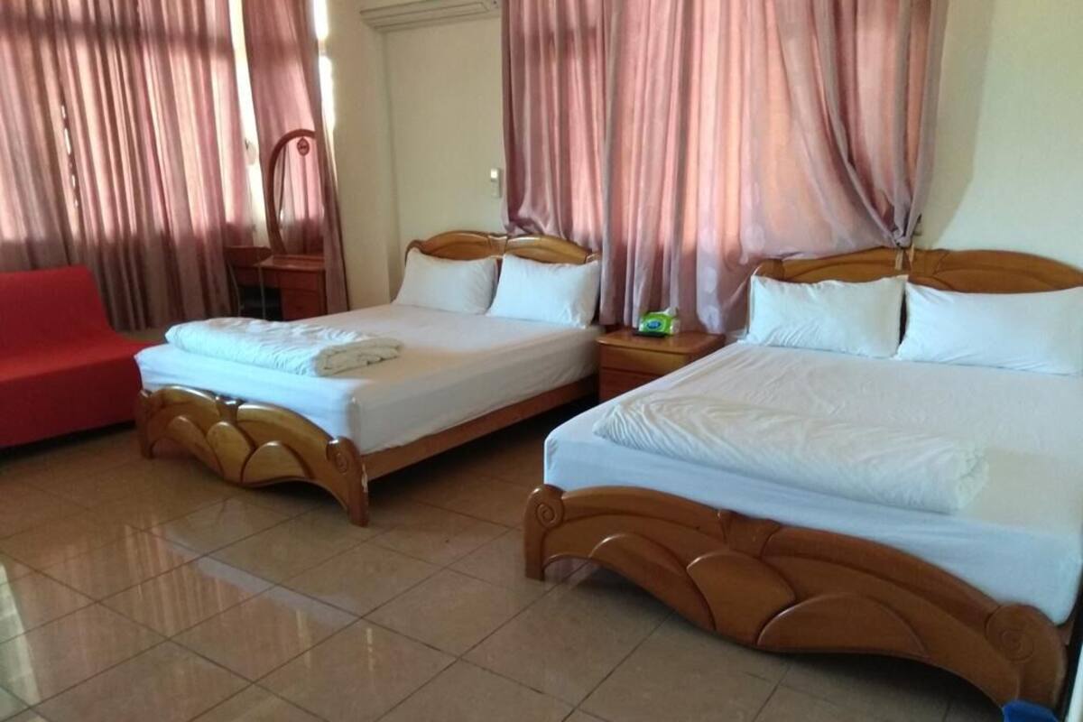A hotel room with two beds, a red chair, and curtains.