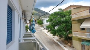 A narrow street with buildings on either side, a balcony with a blue awning, and a mountain in the background. - Pension Gina (Troizinia)