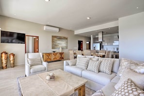 A spacious living room with a large sofa, a coffee table, and a dining area in the background.