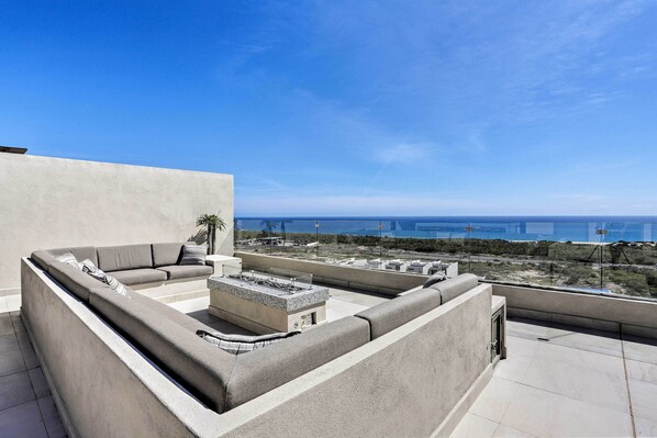 A rooftop terrace with a built-in seating area, a fire pit, and a view of the ocean.