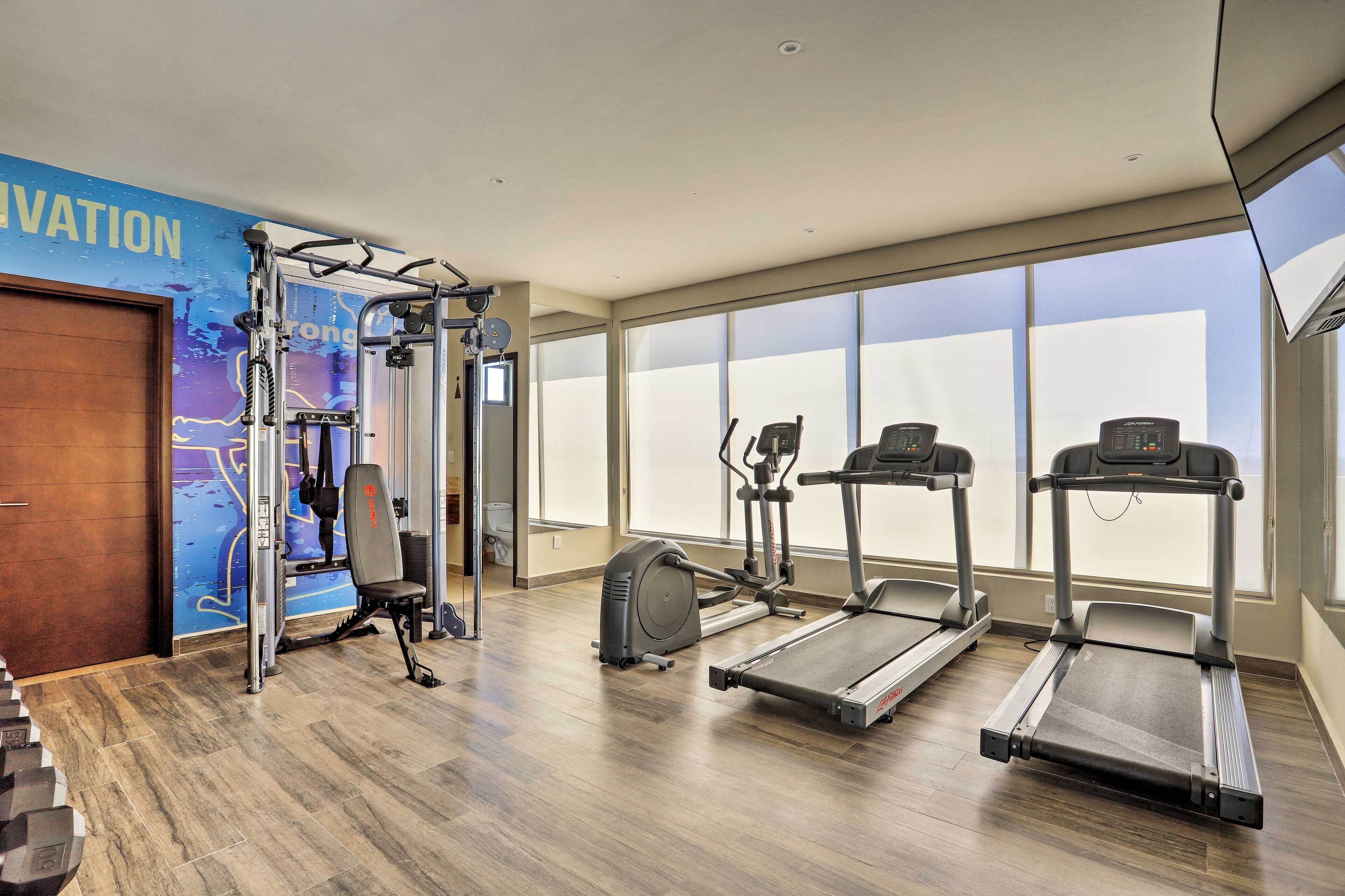 Academia com esteiras, m áquina de pesos e parede com pôster motivacional.