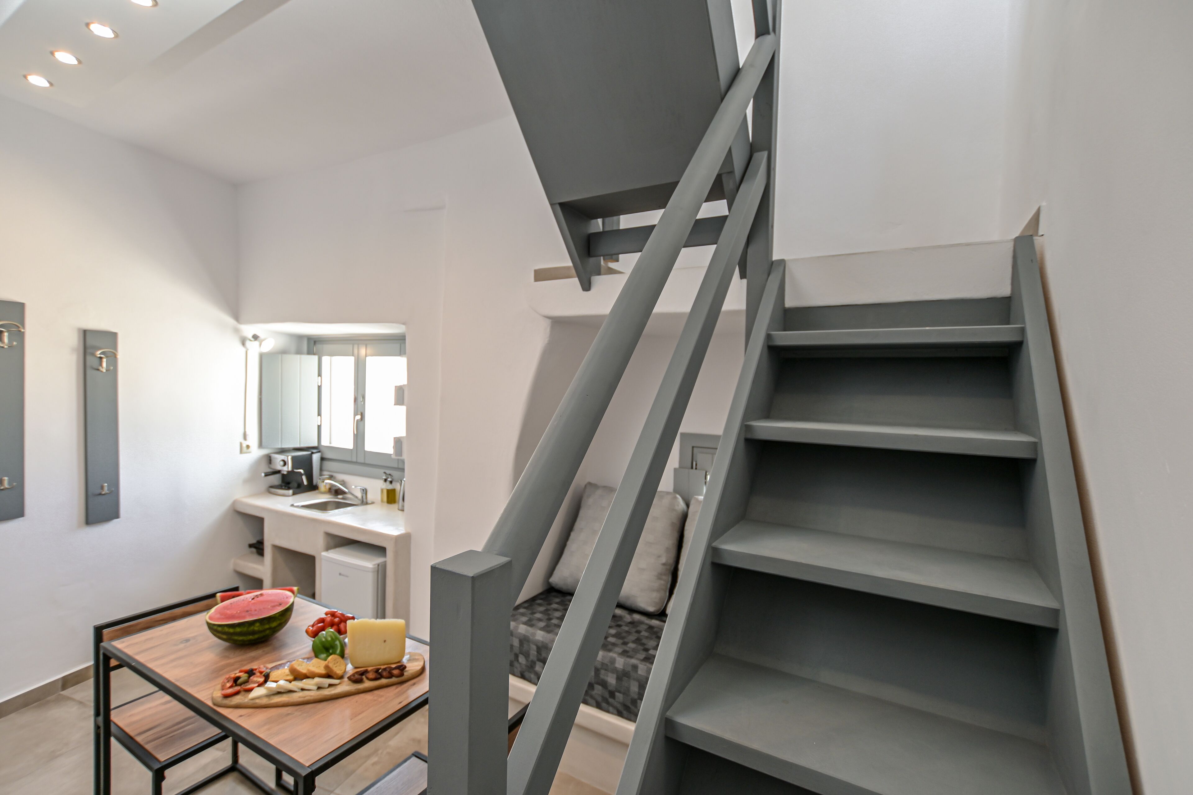 A modern kitchen with a dining table, a watermelon, cheese, and tomatoes.