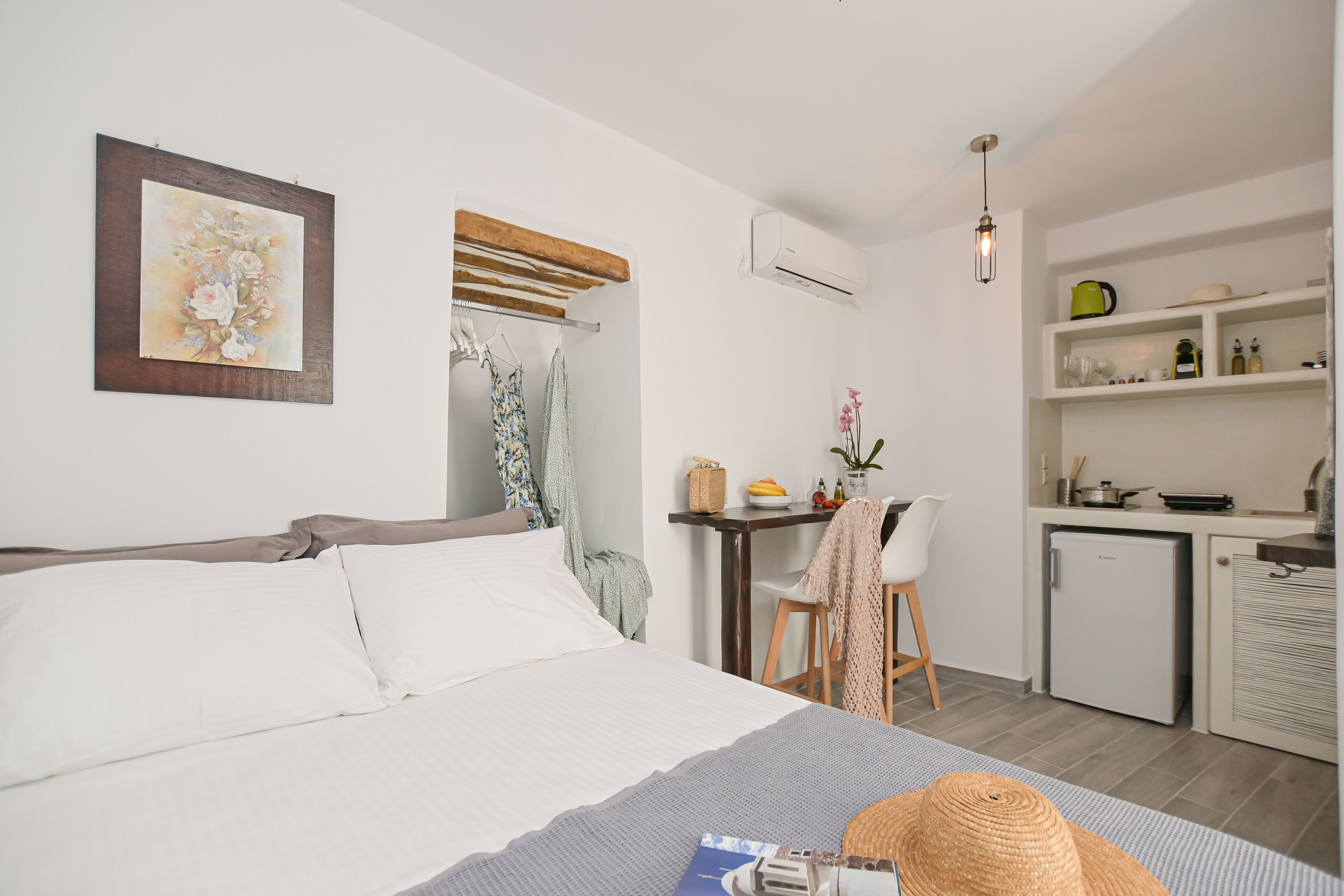 A bedroom with a bed, a desk with a chair, a small kitchenette, and a bathroom with a shower.