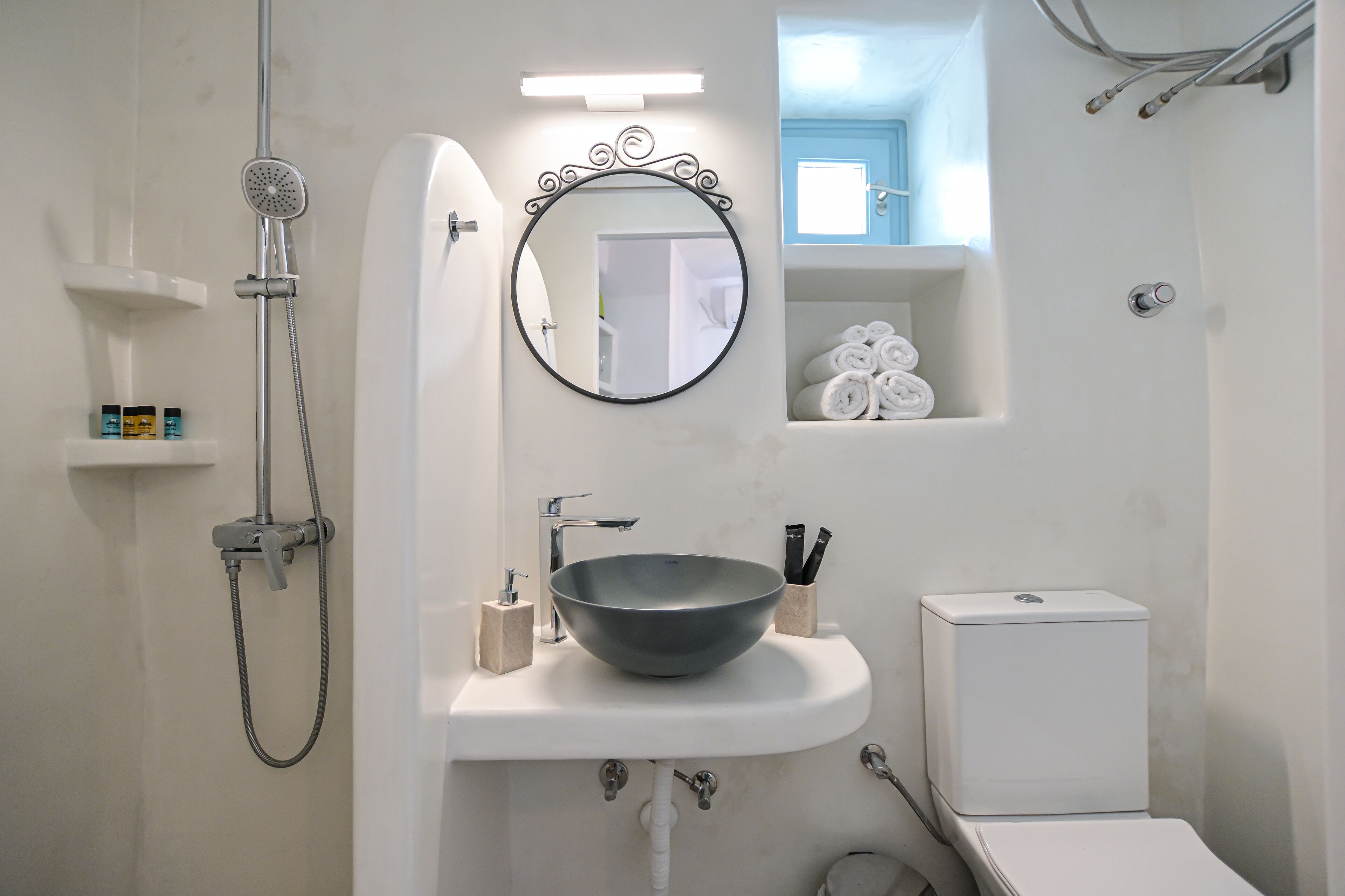 A bathroom with a white sink, a round mirror, a shower, and a toilet.