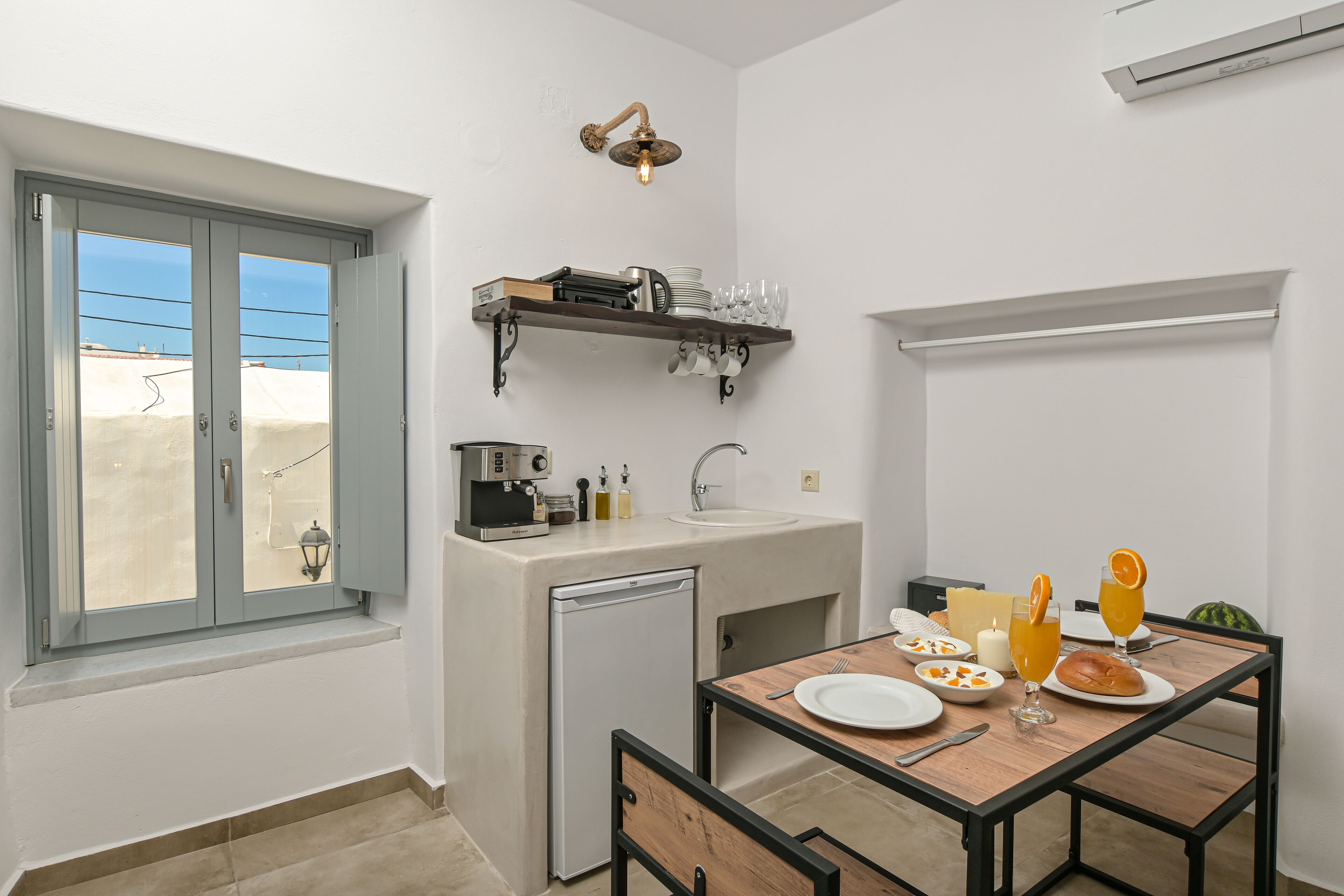 Cocina compacta con lavamanos, un refrigerador pequeño y una zona de comedor con una mesa para dos.