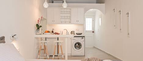 Una cocina funcional con lavadora, zona de comedor con taburetes y cama con un adorno decorativo.