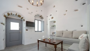 A room with a grey door, a wooden table with candles, a grey sofa, and a TV mounted on the wall. - Venetian Suites (Naxos)