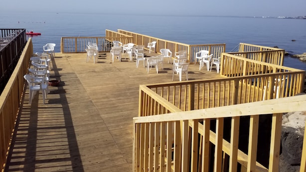 A wooden deck with white plastic chairs and tables, overlooking a calm body of water.