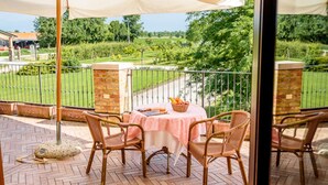 An outdoor patio with a table set for dining, surrounded by wicker chairs, under a large umbrella.