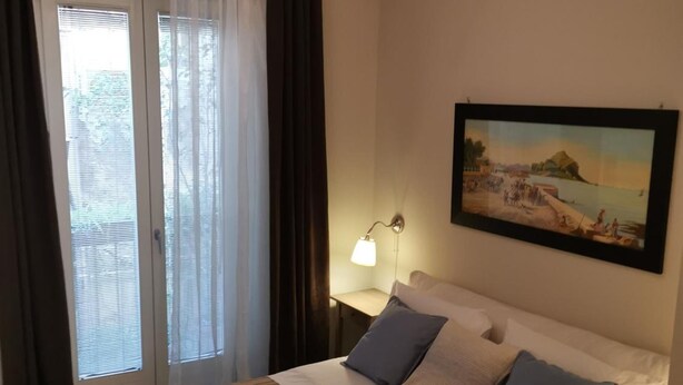 Una camera d'albergo con un letto, un quadro appeso al muro e una finestra con tende.
