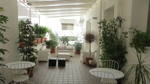 Un’area patio riparata con mobili in vimini bianco, piante in vaso e pavimento piastrellato.