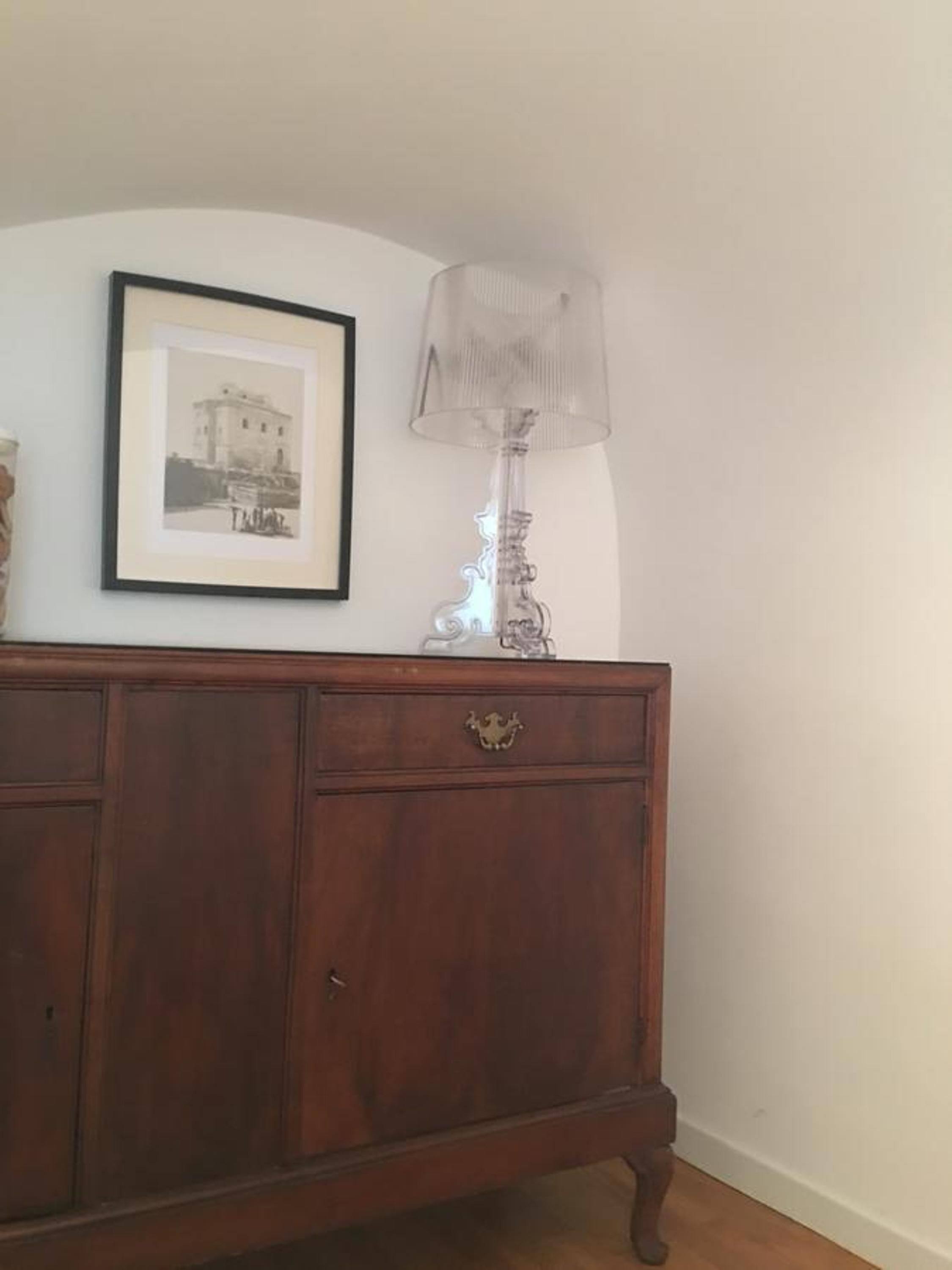 A wooden dresser with a framed picture above it and a clear glass lamp beside it.
