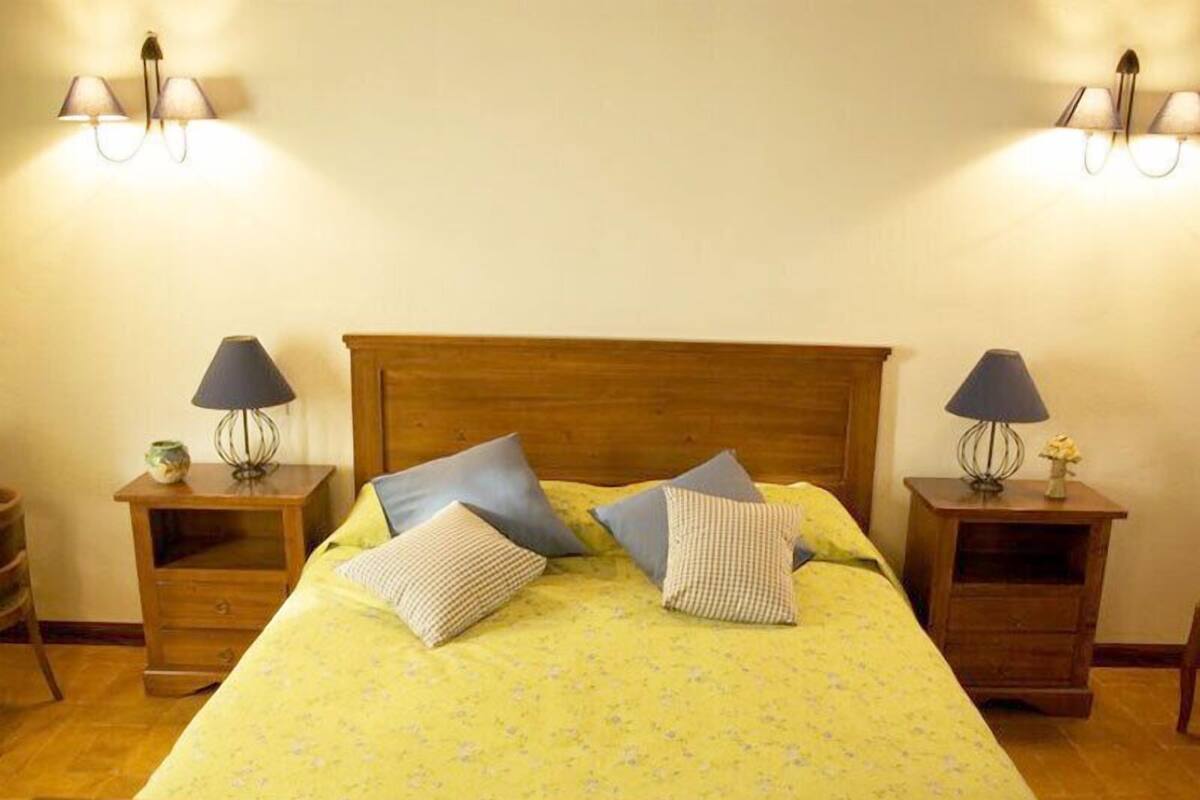 Un lit avec une tête de lit en bois, deux tables de chevet avec des lampes et une couvre-lit à motifs floraux.