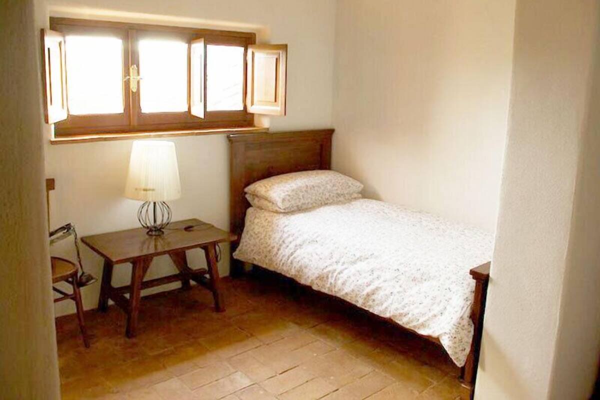 Une petite chambre à coucher avec un lit simple, une table de chevet, une lampe et une fenêtre avec des rideaux.