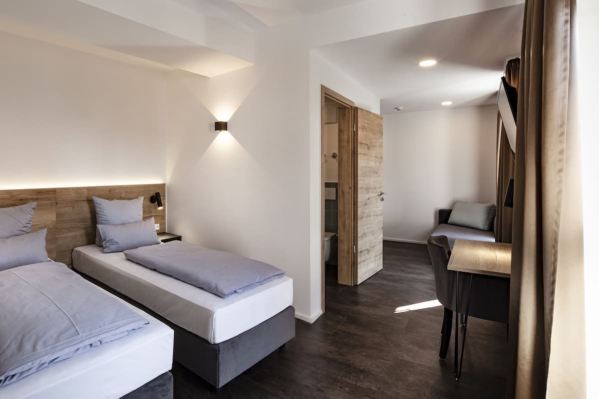 A modern bedroom with two single beds, a wooden headboard, a bedside table, and a small desk with a chair.