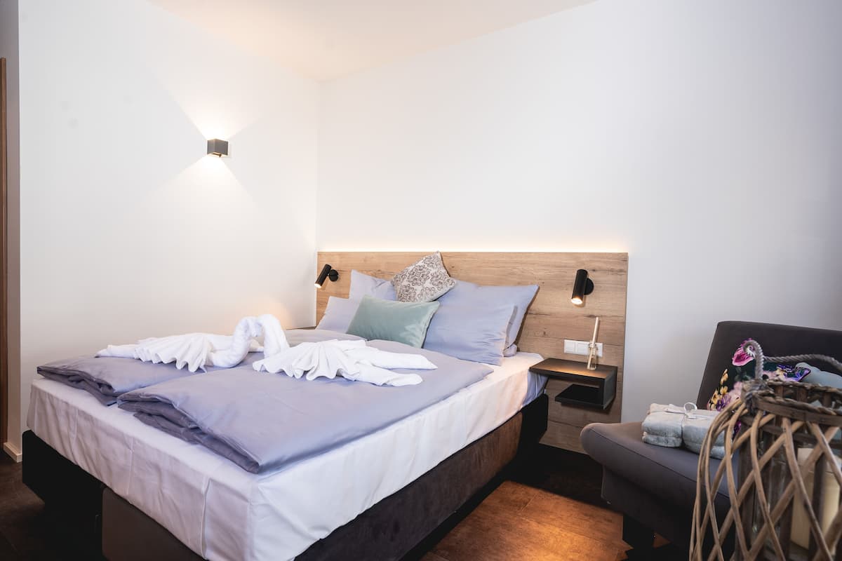 A neatly made bed with pillows and a blanket, a bedside table with a lamp, and a small seating area with a basket.