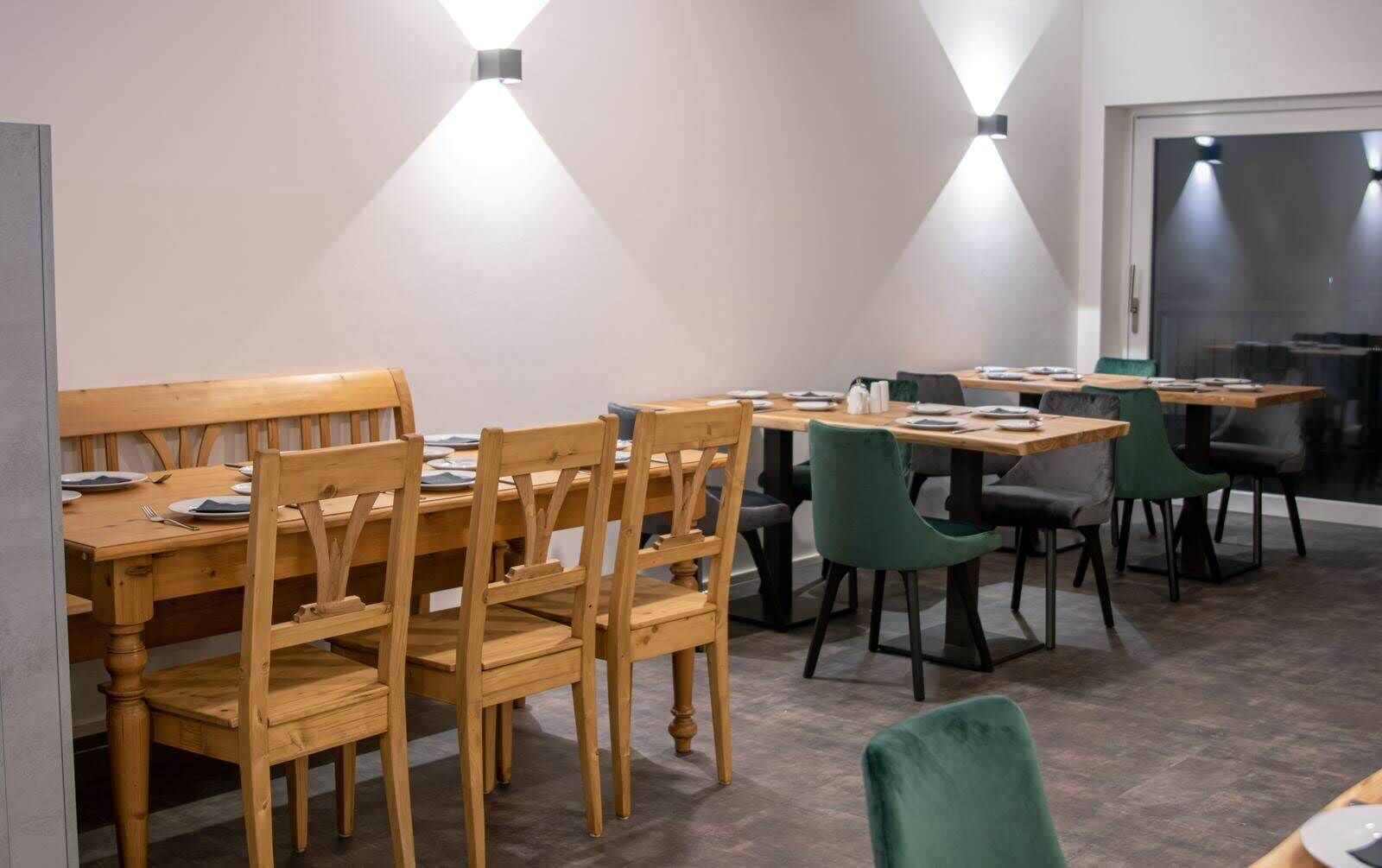 Un comedor con mesas y sillas de madera, dos lámparas fijadas a la pared y una puerta de cristal que da al exterior.