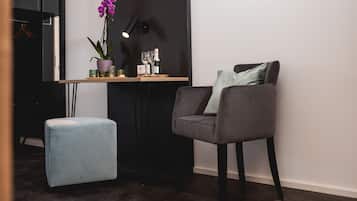 Ein modernes Zimmer mit einem grauen Sessel, einem kleinen blauen Hocker, einer Topforchidee und einem Tisch mit Weingläsern und einer Weinflasche.