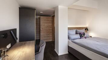 A modern bedroom with a bed, bedside table, and a desk with a lamp.