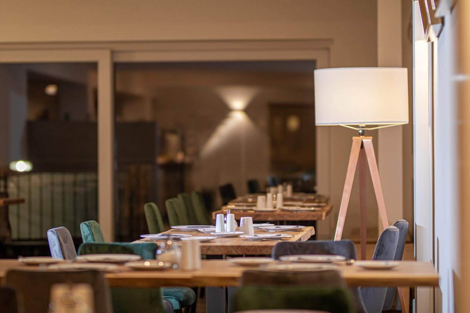 A restaurant with long tables, green chairs, and a floor lamp.