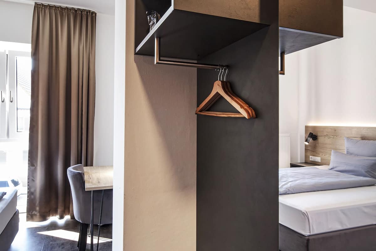 A modern hotel room with a bed, bedside table, and a hanging coat rack.