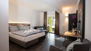A modern bedroom with a bed, bedside table, chair, and a view of the outdoors. - Drexels Parkhotel am Schloss (Krumbach)