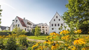 A modern building with a red roof and white walls, surrounded by a well-maintained garden with yellow flowers. - Drexels Parkhotel am Schloss (Krumbach)