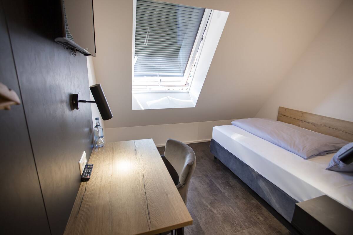 A small, modern room with a wooden desk, a single bed, and a skylight.