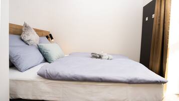 A neatly made bed with a light blue mattress and pillows, a wooden headboard, and a black wardrobe to the right.