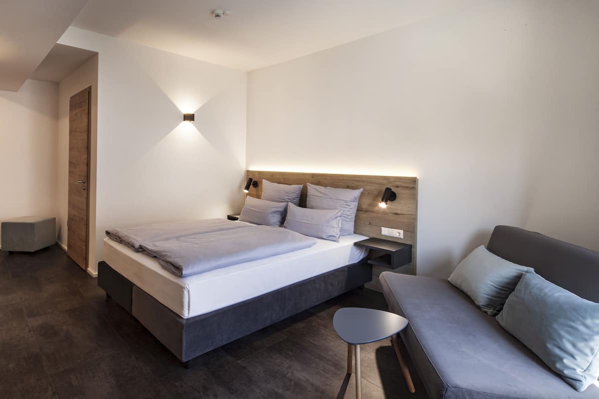 A modern bedroom with a large bed, bedside tables, a small seating area, and a wooden headboard.