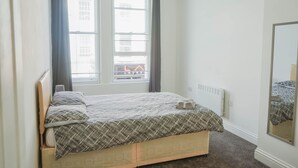 A bedroom with a bed, a window with curtains, a radiator, and a mirror on the wall. - 1 Bed Flat in Pedestrianized High Street (Dover)