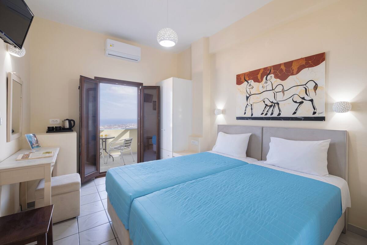 A hotel room with a bed, a desk, a chair, a TV, and a painting on the wall.