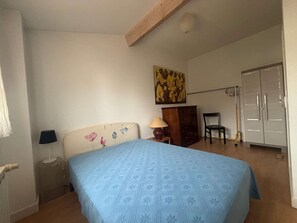 A bedroom with a bed, a nightstand, a lamp, a chair, a wardrobe, and a painting on the wall.