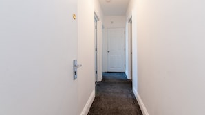 A narrow hallway with white walls and a carpeted floor, leading to a white door at the end. - Studio in Pedestrianized High Street (Dover)