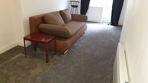 A living room with a brown sofa, a small wooden table, and a chair. - Studio in Pedestrianized High Street (Dover)