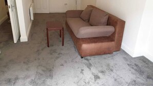 A living room with a brown sofa, a small wooden table, and a white door in the background. - Studio in Pedestrianized High Street (Dover)