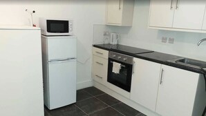 A compact kitchen with white cabinets, a microwave, a stove, and a sink. - Studio in Pedestrianized High Street (Dover)