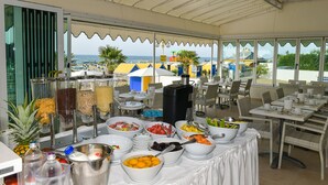 A buffet setup with various food items and a view of the beach and buildings in the background. - Hotel Souvenir (Jesolo)