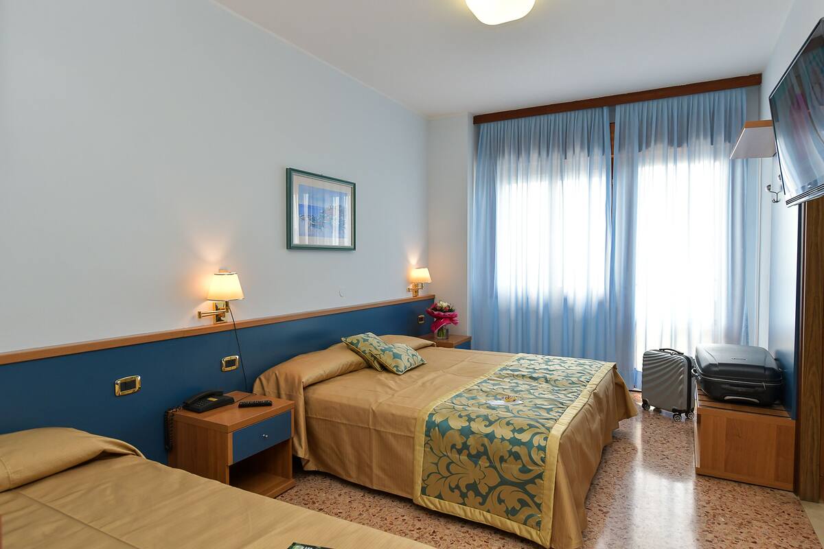 A hotel room with two beds, a desk, a chair, a TV, and a window with curtains.